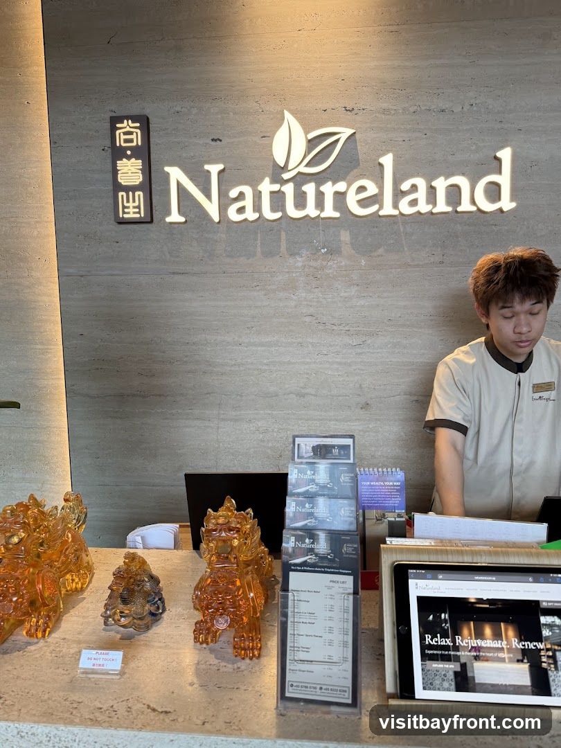 A reception desk with the Natureland logo prominently displayed on the wall. A staff member stands behind the desk. On the desk are decorative figurines, brochures, a price list, and a tablet displaying the Natureland website.