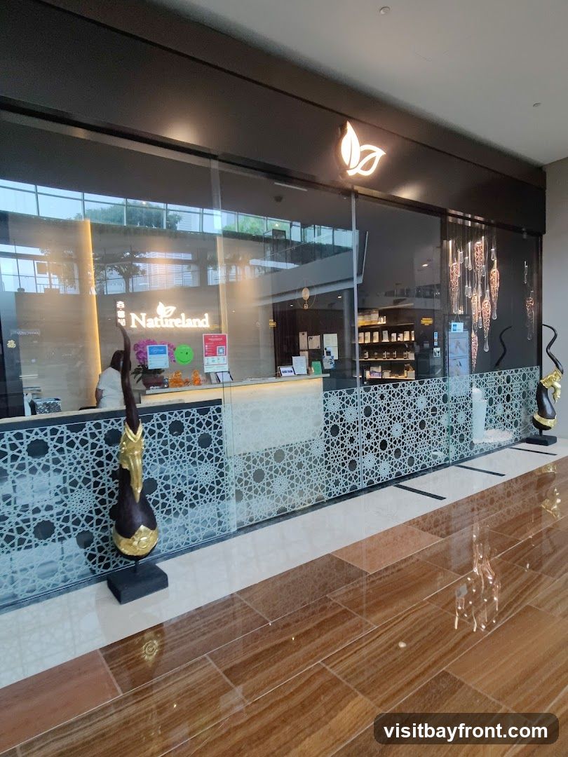 A wide shot of the Natureland storefront, featuring a large glass window with the Natureland logo and name prominently displayed. Inside, a reception desk is visible with a person behind it. The interior shows shelves stocked with products. Decorative elements, including a sculpture and hanging lights, add to the ambiance. The floor is made of polished wood-like tiles.
