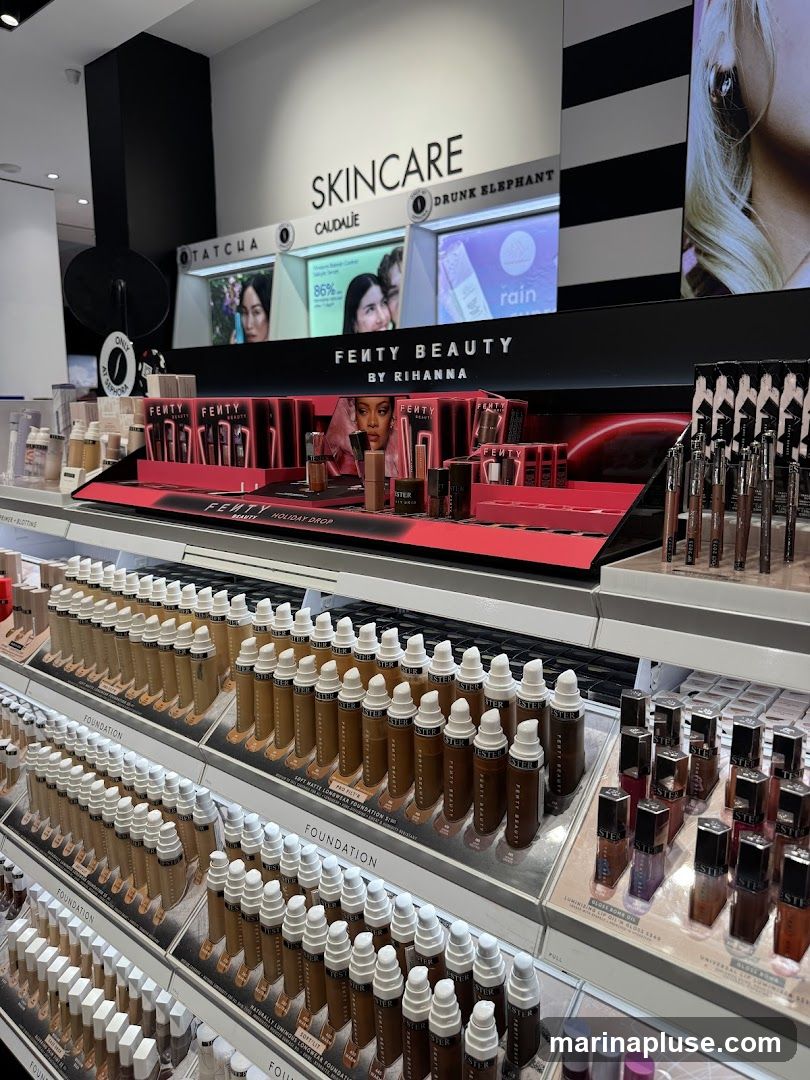 A display of Fenty Beauty products, primarily foundations and lip glosses, is shown in a retail setting. The display features rows of foundation bottles in various shades, with labels indicating "FOUNDATION" and specific product names like "SOFT MATTE LONGWEAR FOUNDATION" and "PRO FILT'R". Above the foundation display, there is a section dedicated to "FENTY BEAUTY BY RIHANNA" with smaller product packaging. In the background, a "SKINCARE" section is visible with brands like Caudalie and Drunk Elephant.