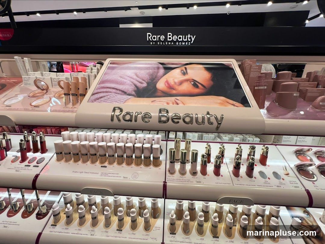 A display of Rare Beauty makeup products, including foundations, blushes, and lip products. The display features a large image of Selena Gomez and the brand's logo.