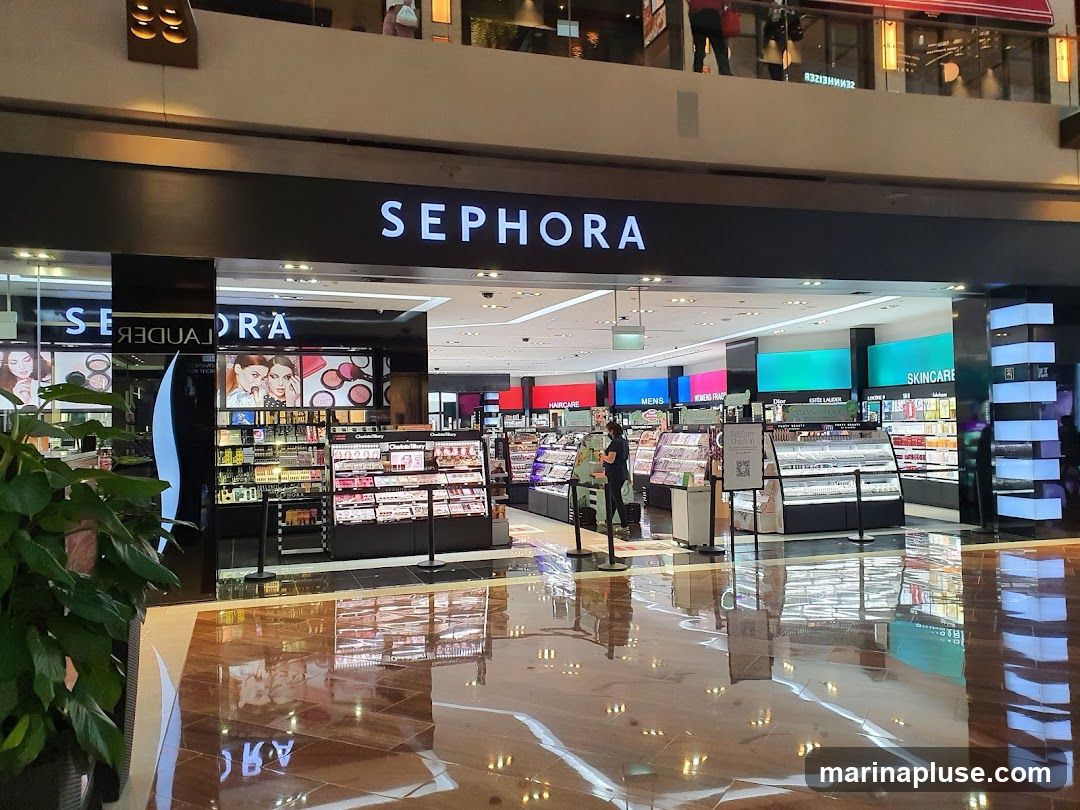 The exterior of a Sephora store is shown, with the brand name prominently displayed above the entrance. The store is filled with shelves of makeup, skincare, and other beauty products. The floor is highly reflective, mirroring the store's interior.