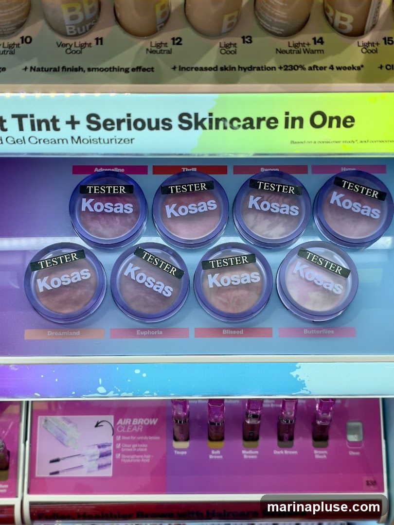 A display of Kosas makeup products, including BB Burst foundation testers and Air Brow Clear. The display features various shades and product names like 'Adrenaline', 'Thrill', 'Swoon', 'Dreamland', 'Euphoria', and 'Blissed'. Below, Air Brow Clear is shown with shades like 'Taupe', 'Soft Brown', 'Medium Brown', 'Dark Brown', 'Brown Black', and 'Clear'.