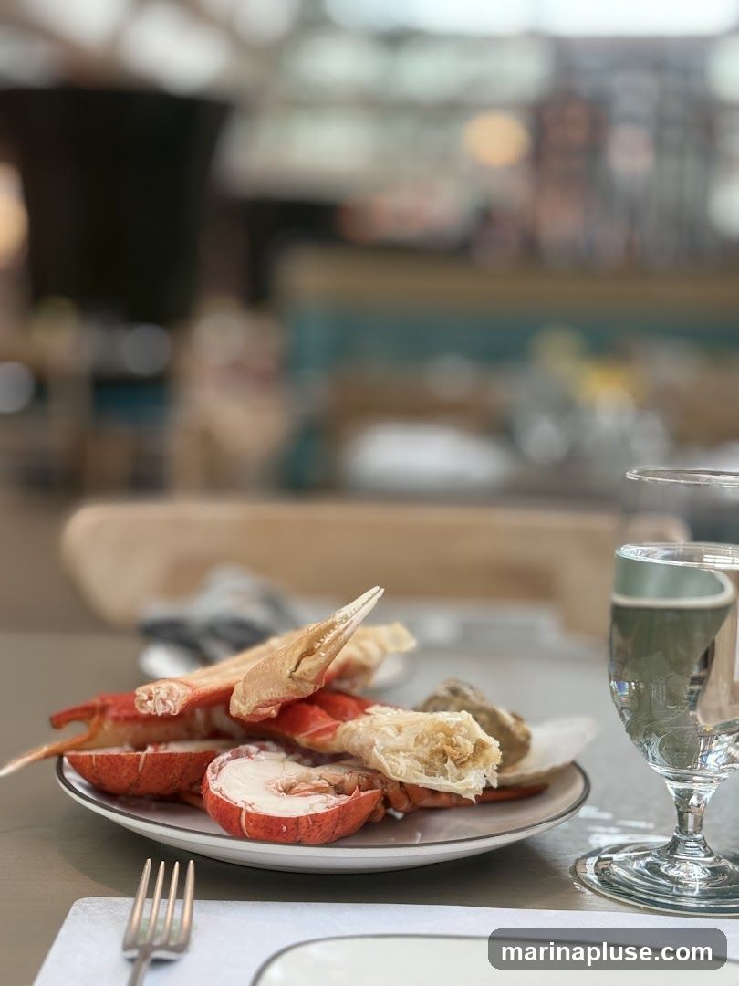 A plate of cooked lobster and crab legs sits on a table, next to a glass of water. The background is blurred, showing the interior of a restaurant with tables and chairs.