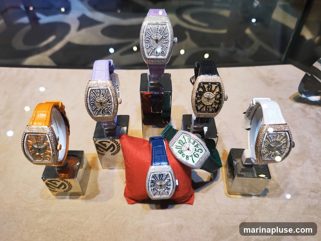 A display of seven luxury watches, each featuring diamond-encrusted bezels and faces. The watches have various colored straps, including orange, purple, black, white, blue, and green. They are showcased on individual stands, with some prices visible: $57,500 and $41,500. The background appears to be a store display with reflections.