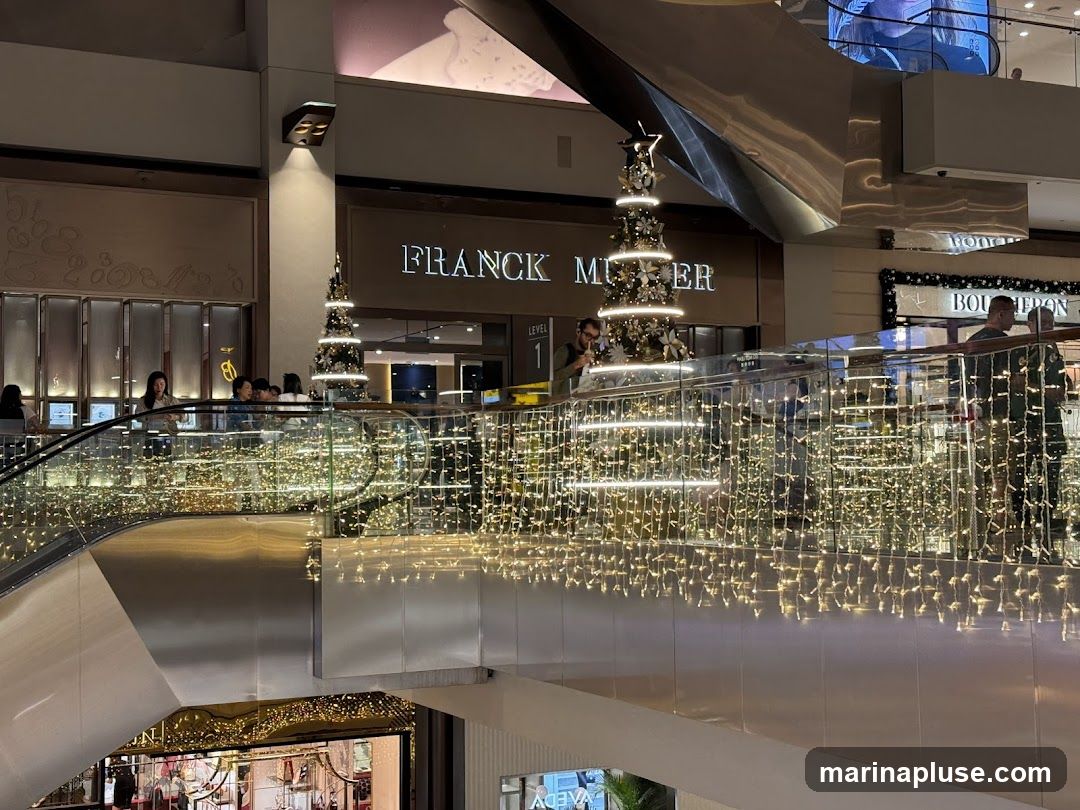 A view of the Franck Muller store in a shopping mall, decorated for Christmas with trees and string lights. People are visible on escalators and walkways.