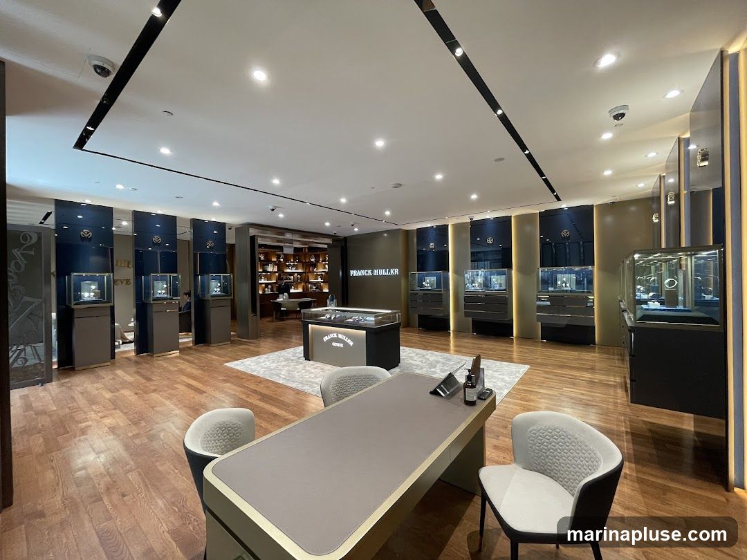 The interior of a Franck Muller watch store, featuring display cases with watches, a central counter, and seating areas. The store has a luxurious and modern design with wooden floors and elegant lighting.