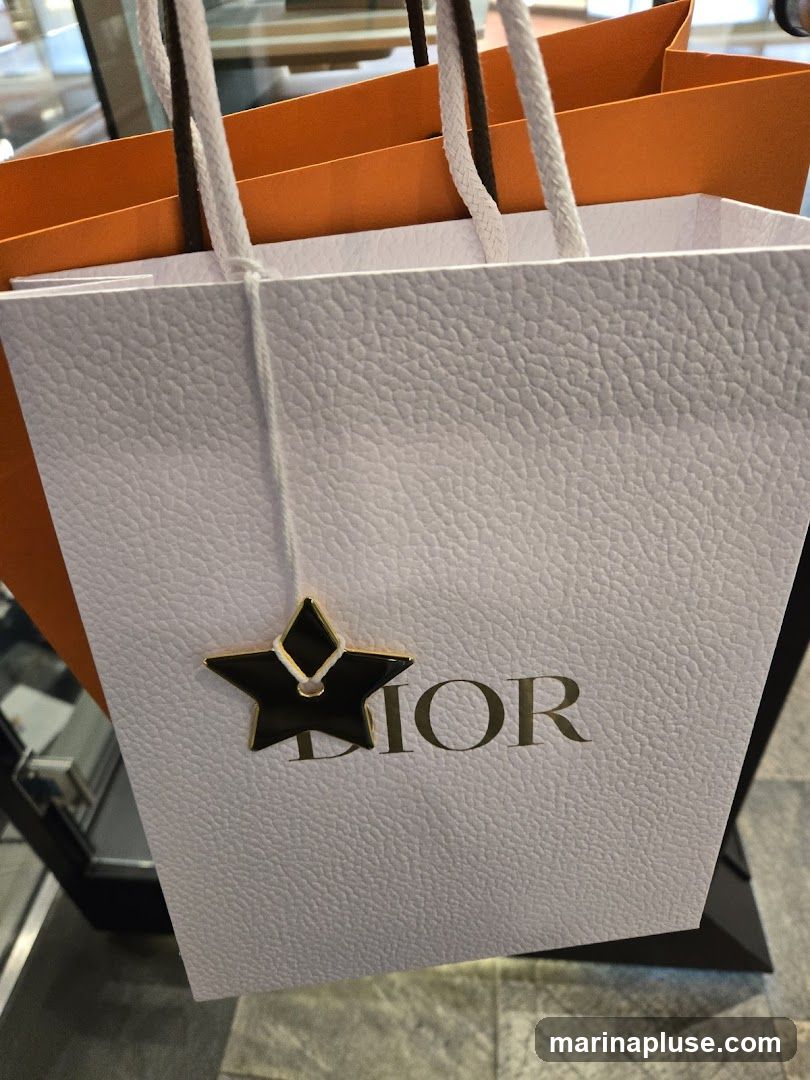 A close-up of two textured shopping bags, one white and one orange, with the Dior logo visible on the white bag. A star-shaped charm with a diamond detail hangs from the white bag's string.