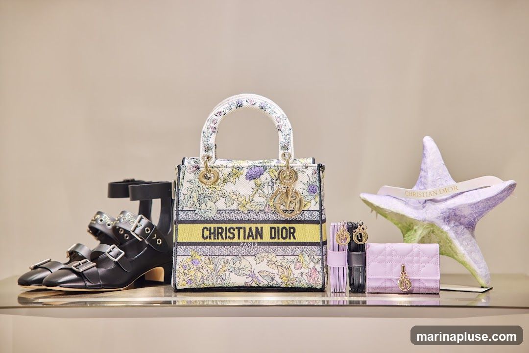 A display of Christian Dior products including black leather heels with multiple buckles, a floral print handbag with yellow trim and the Christian Dior Paris logo, a lavender quilted cardholder, and a decorative purple starburst sculpture with the Christian Dior logo on a white ribbon.