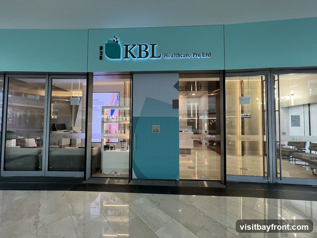 The exterior of a KBL Healthcare Pte Ltd clinic. The storefront features large glass doors and windows, with the company logo and name prominently displayed above the entrance. Inside, shelves stocked with various products are visible, along with a reception area and seating.