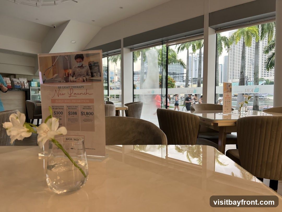 A promotional display for BB Light Therapy is set up on a table in a well-lit room with large windows overlooking a city skyline and palm trees. The display features an "Early Bird Promotion" with prices for different treatments. The room appears to be a waiting area or lounge, with comfortable seating and a vase of flowers on the table.