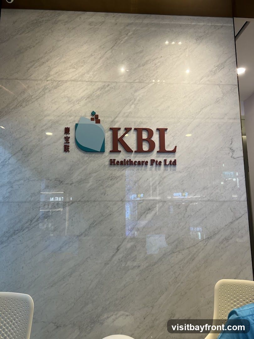 A close-up shot of a marble wall with the KBL Healthcare Pte Ltd logo prominently displayed. The logo features stylized text and a graphic element. Reflections of lights and possibly other signage are visible on the polished surface.