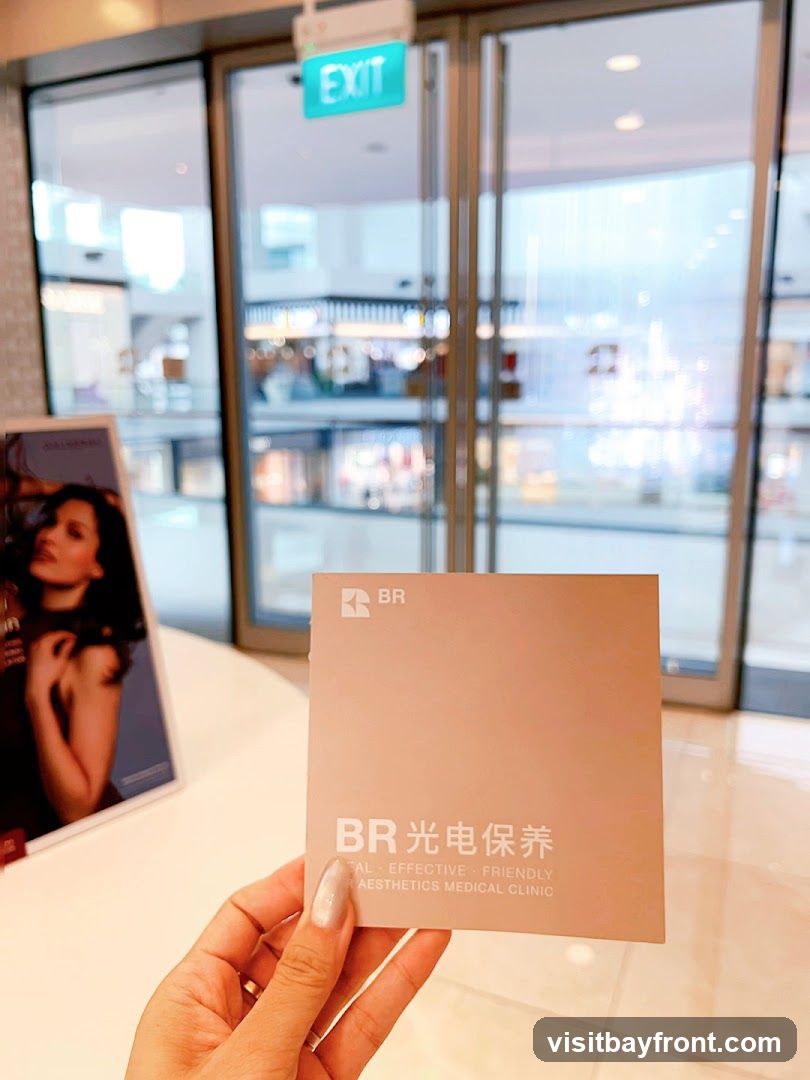 A hand holds a light pink brochure with the BR logo and Chinese characters for "Light Electric Maintenance" on it. Below this, it reads "REAL EFFECTIVE FRIENDLY AESTHETICS MEDICAL CLINIC". To the left, a poster of a woman is visible. The background shows a blurred view of a shopping mall interior with glass doors and an exit sign.