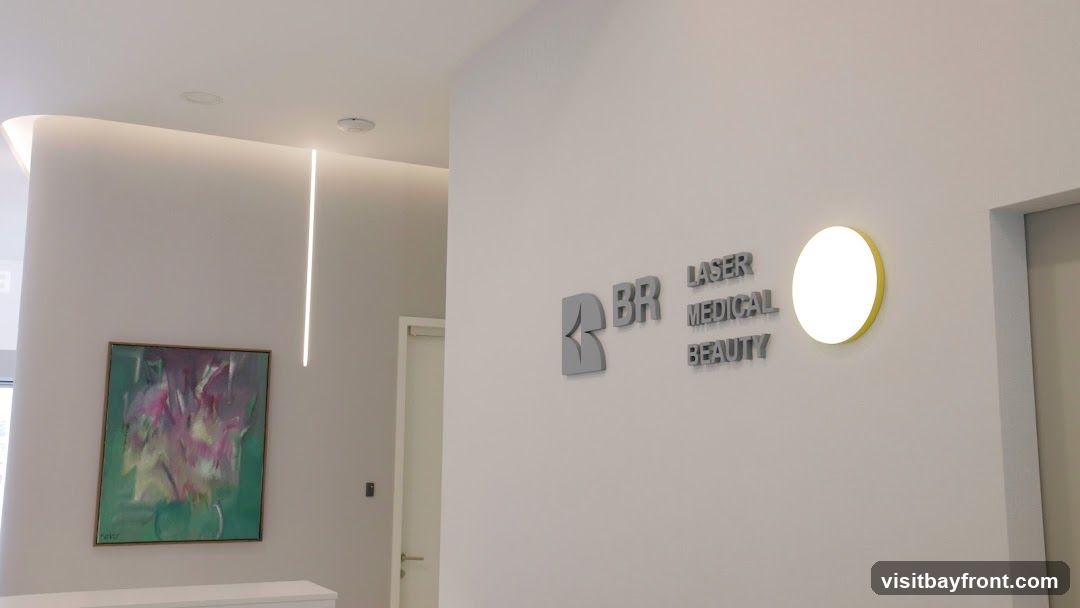 The image shows the interior of a modern medical beauty clinic. A sign on the wall reads "BR LASER MEDICAL BEAUTY". There is a framed abstract painting on the wall and a circular light fixture. The space appears clean and well-lit with recessed lighting and a vertical light strip.