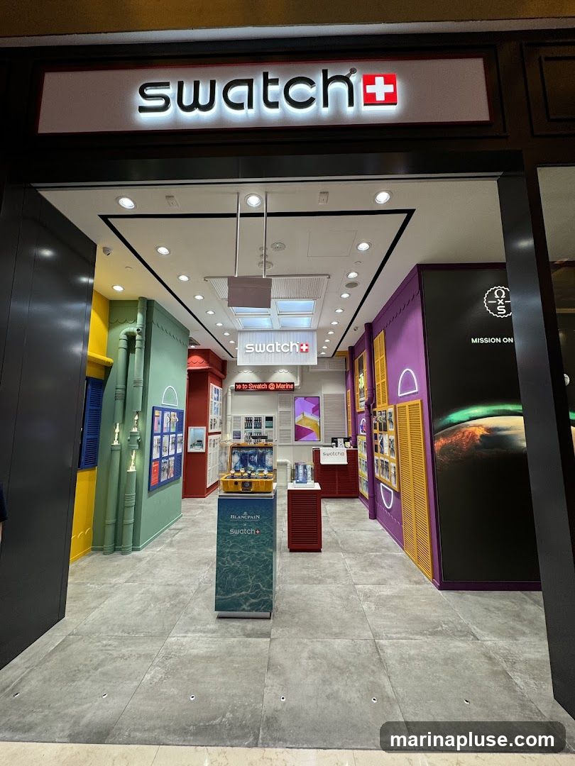 The exterior of a Swatch store is visible, with the prominent "swatch+" logo above the entrance. Inside, the store is brightly lit and displays watches on various stands and shelves. The interior features colorful walls and decorative elements, creating a vibrant atmosphere. A display case showcases a collection of watches, and promotional materials are visible throughout the store.