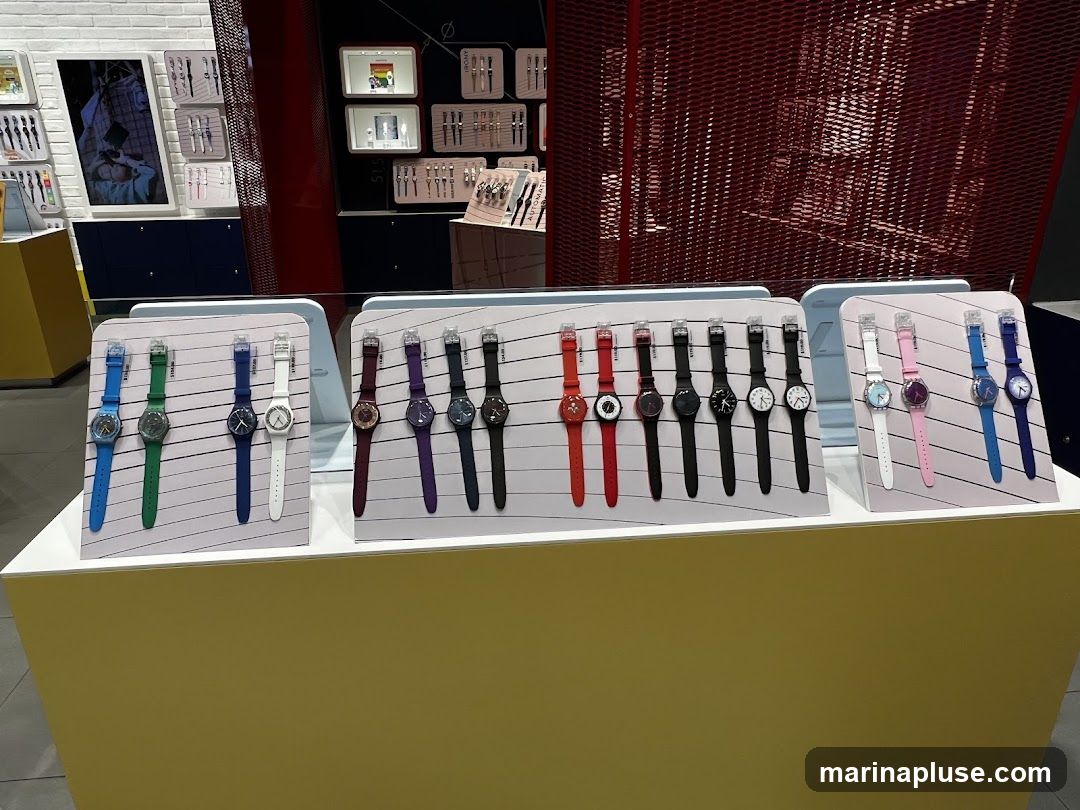 A display of various Swatch watches on stands, with different colors and styles. The watches are arranged in rows on white stands, with prices visible on some. In the background, there are shelves with more watches and promotional materials.