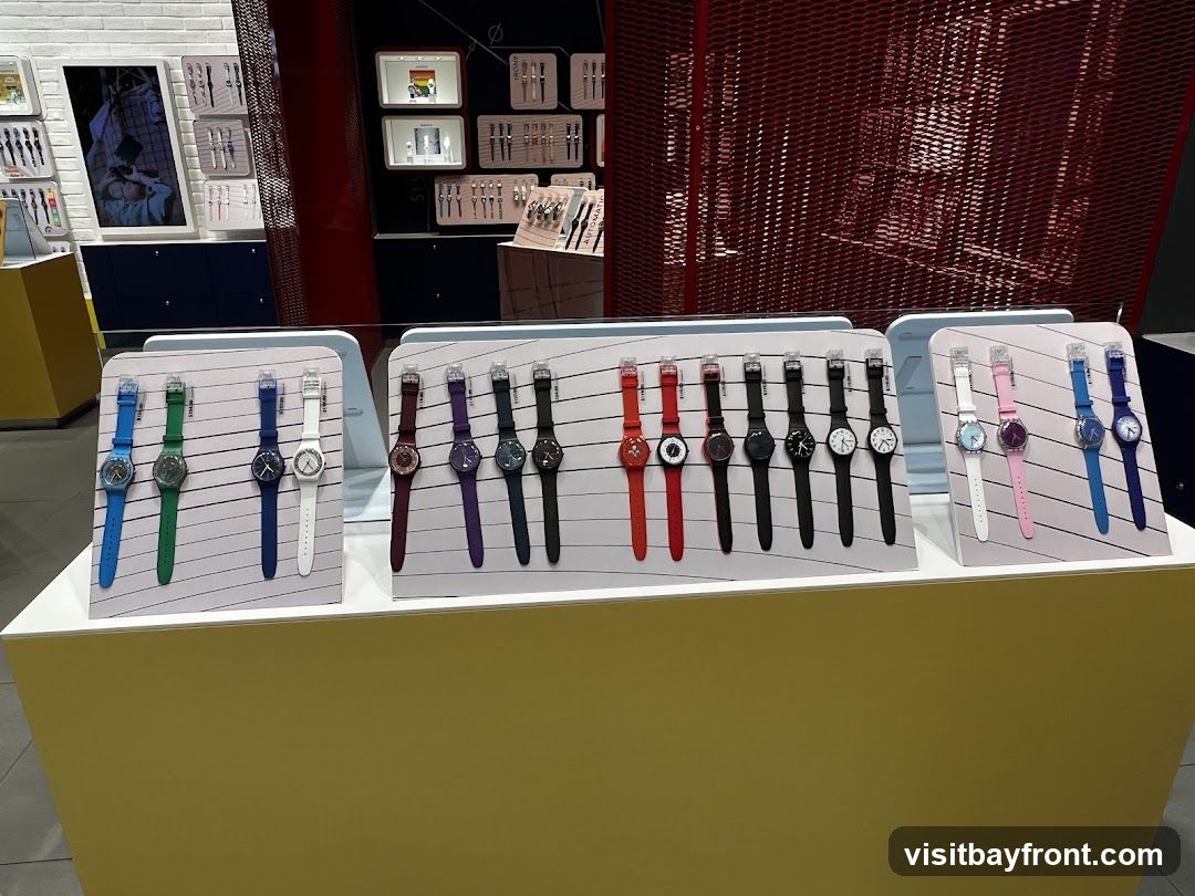 A display of various Swatch watches on stands, with different colors and styles. The watches are arranged in rows on white stands, with prices visible on some. In the background, there are shelves with more watches and promotional materials.
