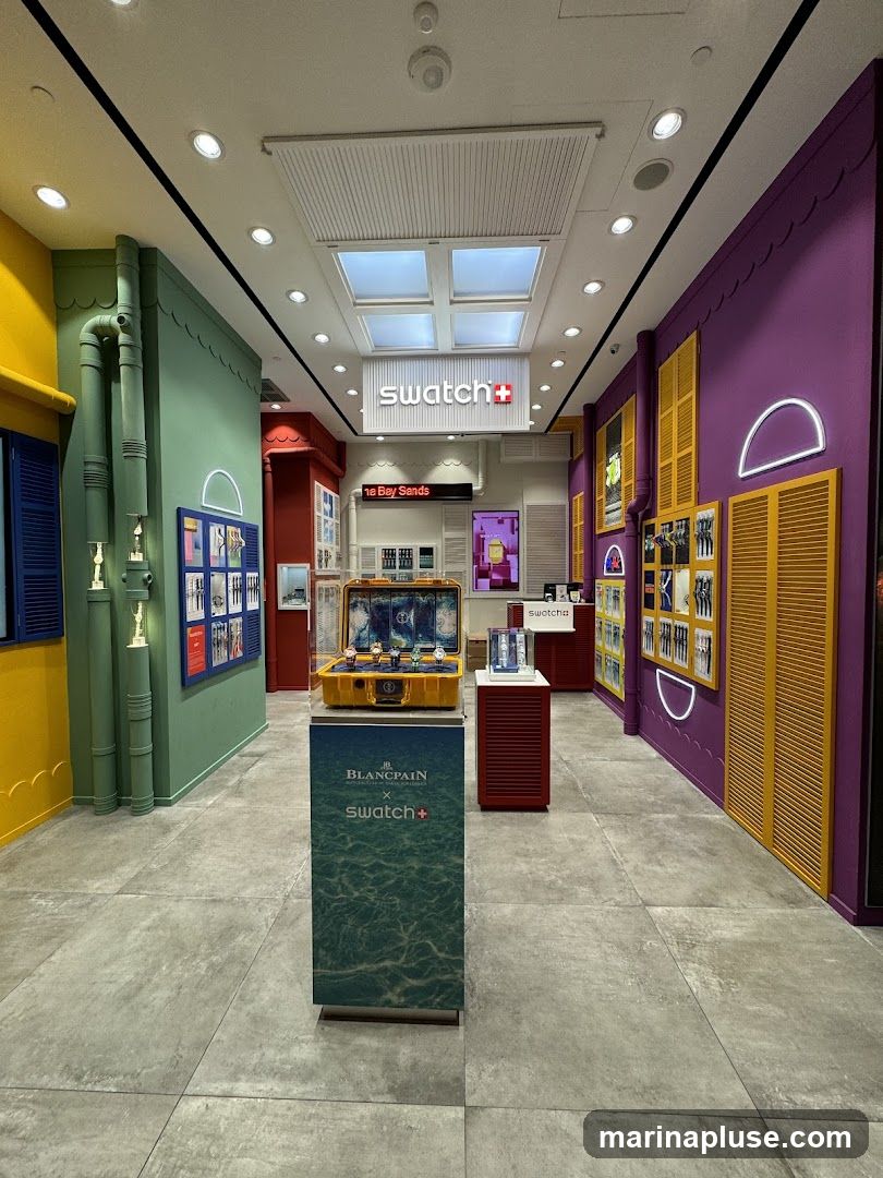 The interior of a colorful Swatch store. The walls are painted in vibrant yellow, green, and purple. Displays showcase watches and accessories. A prominent Swatch logo is visible on the ceiling. A display case features a yellow box with watches inside, alongside a stand with a Blancpain x Swatch collaboration advertisement.