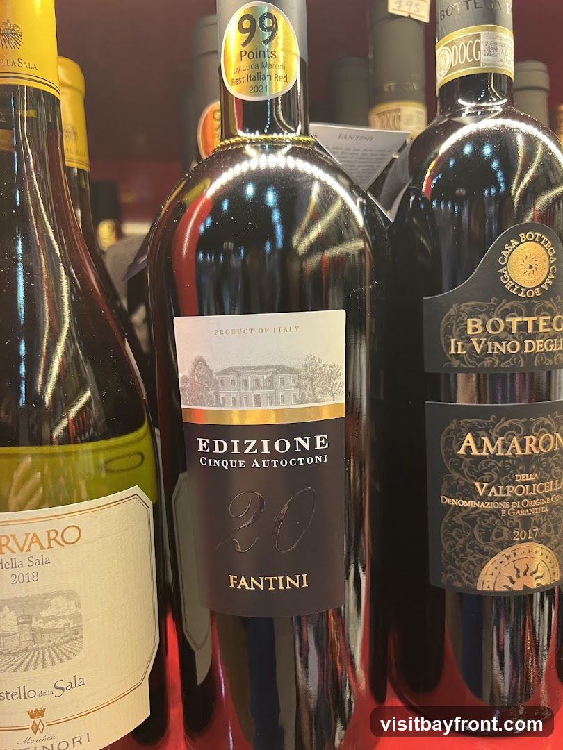 Several bottles of Italian red wine are displayed on a shelf. One bottle in the center is labeled "EDIZIONE CINQUE AUTOCTONI 20 FANTINI" and has a sticker indicating "99 Points by Luca Maroni Best Italian Red 2021". To its right is a bottle of "AMARONE DELLA VALPOLICELLA 2017". To the left is a bottle labeled "RVARO della Sala 2018" with a yellow cap.