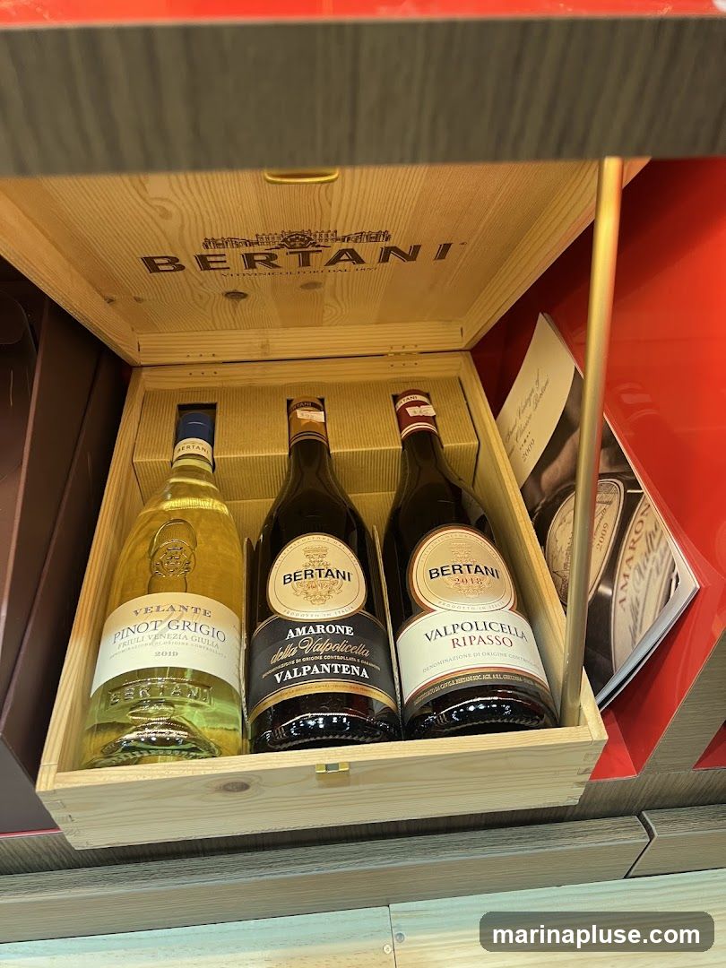 A wooden gift box containing three bottles of Bertani wine. The box is open, revealing the bottles inside. The lid of the box is engraved with the Bertani logo and name. The bottles are: Velante Pinot Grigio 2010, Amarone della Valpolicella Valpantena, and Valpolicella Ripasso 2018. A brochure or booklet is visible to the right of the bottles.
