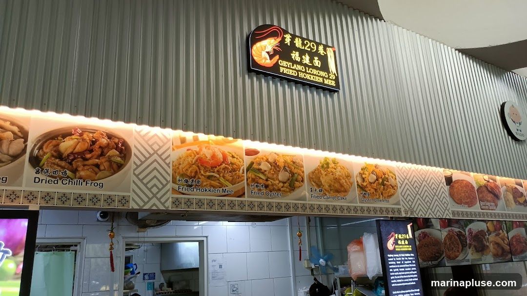 A food stall with a prominent sign for Geylang Lorong 29 Fried Hokkien Mee. The menu features images and names of various dishes including Dried Chilli Frog, Fried Hokkien Mee, Fried Oyster, Fried Carrot Cake, and Oyster Omelette.