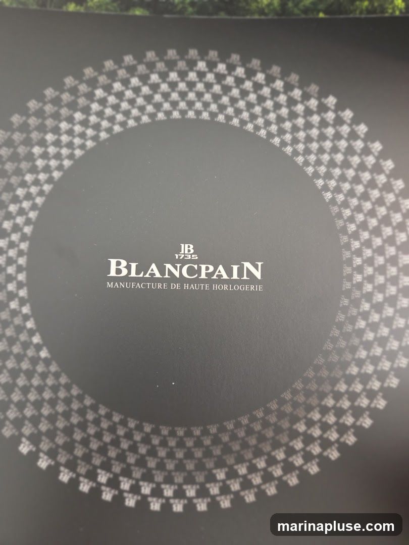 A dark gray background with a circular pattern of repeating logos and text. The central text reads "JB 1735 BLANCPAIN MANUFACTURE DE HAUTE HORLOGERIE". The circular pattern consists of many small "JB" logos and the year "1735" repeated.