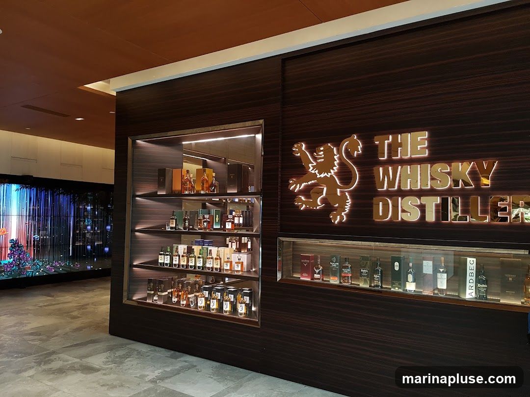 A display case filled with bottles of whisky and other spirits, with the store's name and logo prominently displayed above. The store appears to be modern and well-lit, with a dark wood finish. In the background, a large digital screen displays a colorful, abstract image.