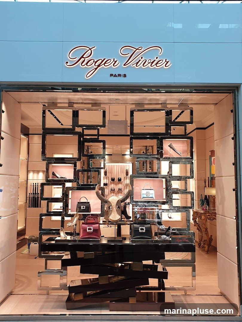 The storefront of a Roger Vivier Paris boutique. The store features a large display window showcasing various handbags and shoes. The brand name 'Roger Vivier PARIS' is prominently displayed in script lettering above the window. The interior of the store is visible, with shelves displaying more merchandise.