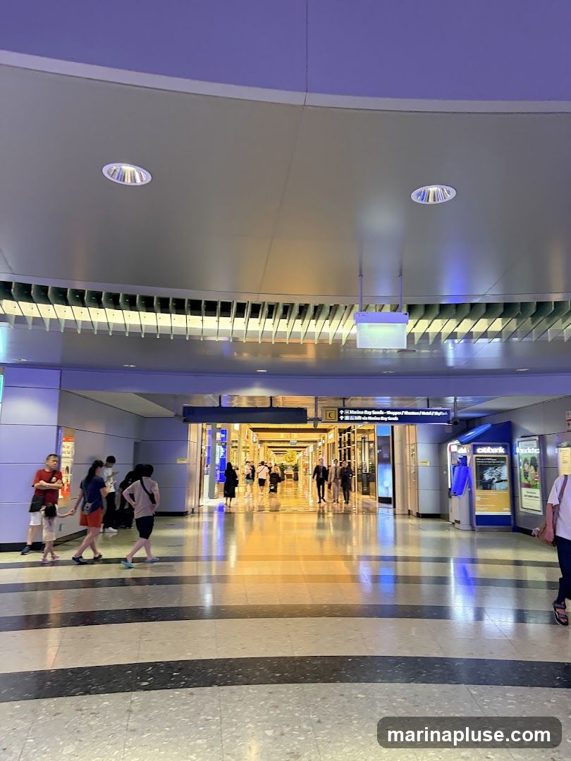 A wide, modern airport terminal hallway with a curved ceiling and bright lighting. People are walking in both directions. Shops and information signs are visible in the distance. A Citibank ATM is on the right.