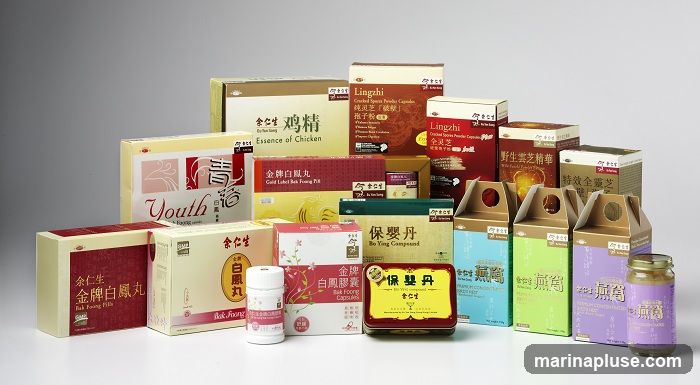 A collection of various health and wellness products, including boxes and jars, are displayed against a plain background. The products feature Chinese and English labeling, with some indicating ingredients like 'Essence of Chicken', 'Lingzhi', 'Bak Foong Pills', and 'Bo Ying Compound'. The packaging varies in color and design, with some boxes having intricate patterns and others featuring simple text and imagery.