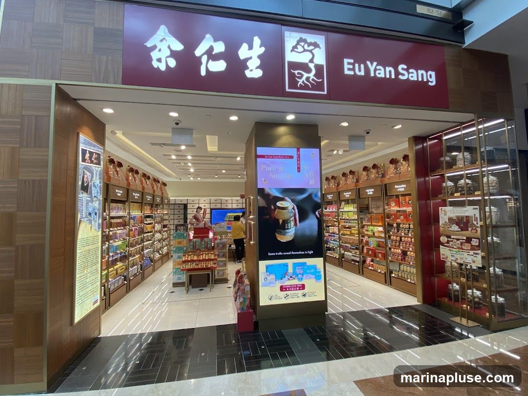 The exterior of a Eu Yan Sang store, featuring its prominent signage with Chinese characters and the English name "Eu Yan Sang" above the entrance. The store is well-lit and displays a wide variety of products on shelves lining the interior. A digital screen near the entrance shows promotional content.