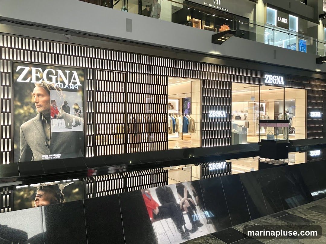 The exterior of a Zegna store with large advertisements and displays of clothing visible through the windows. The store features a modern design with illuminated vertical elements.