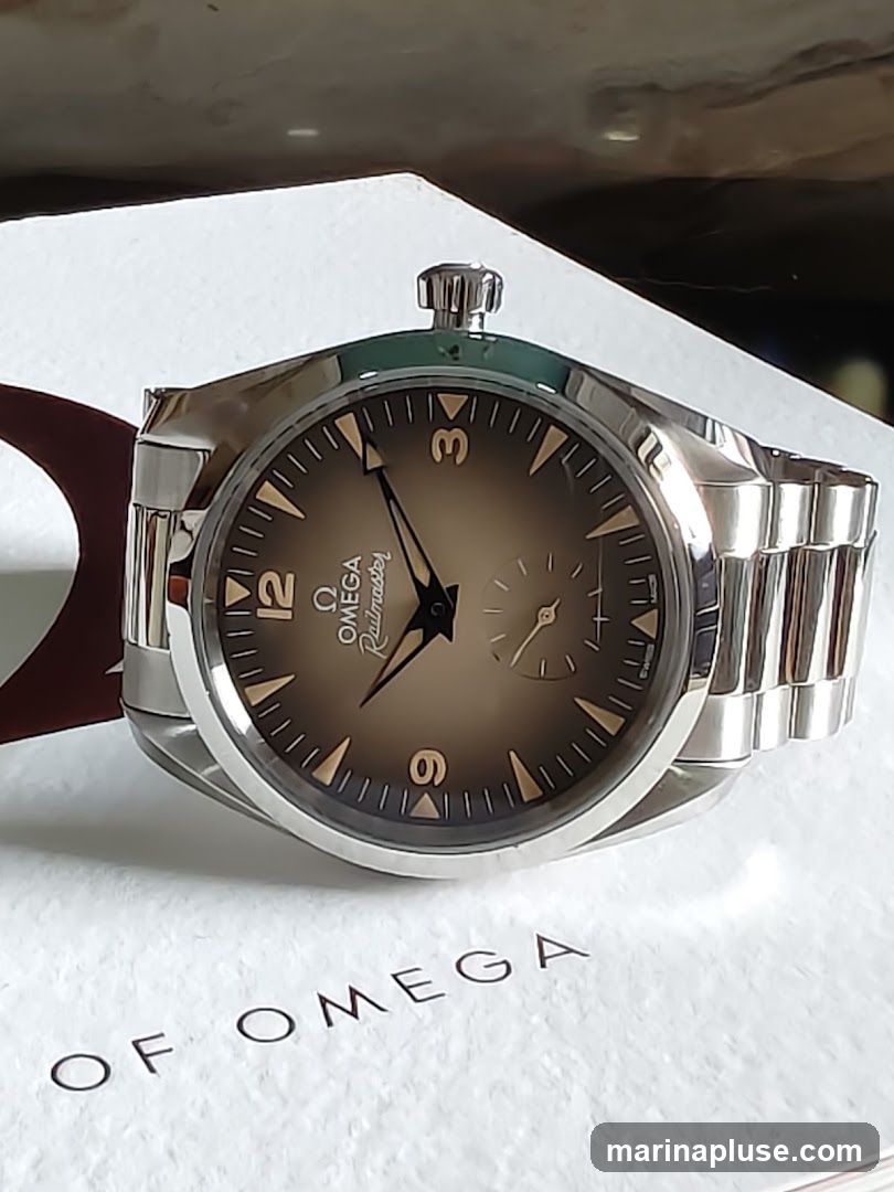 A close-up shot of an Omega Railmaster watch with a brown dial and silver bracelet. The watch is resting on a white surface with the words "OF OMEGA" printed on it.