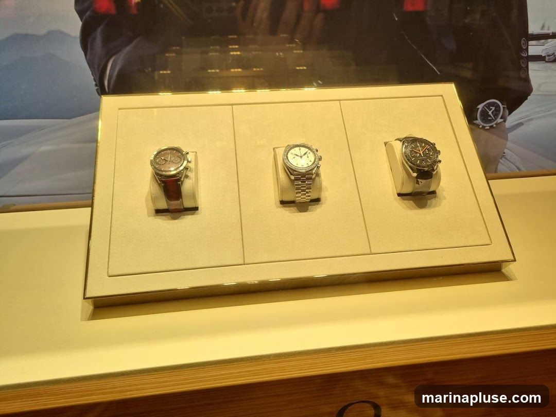 A display case shows three watches. The watch on the left has a brown leather strap. The middle watch has a silver metal band. The watch on the right has a black strap. Behind the watches is a large advertisement featuring a person in a suit.
