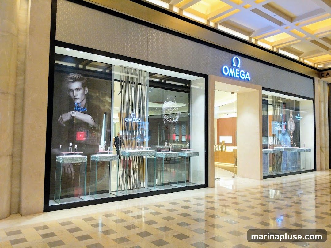 The exterior of an Omega watch store. The storefront features large glass windows displaying watches and a large advertisement of a man wearing a watch. The Omega logo and name are prominently displayed above the entrance.