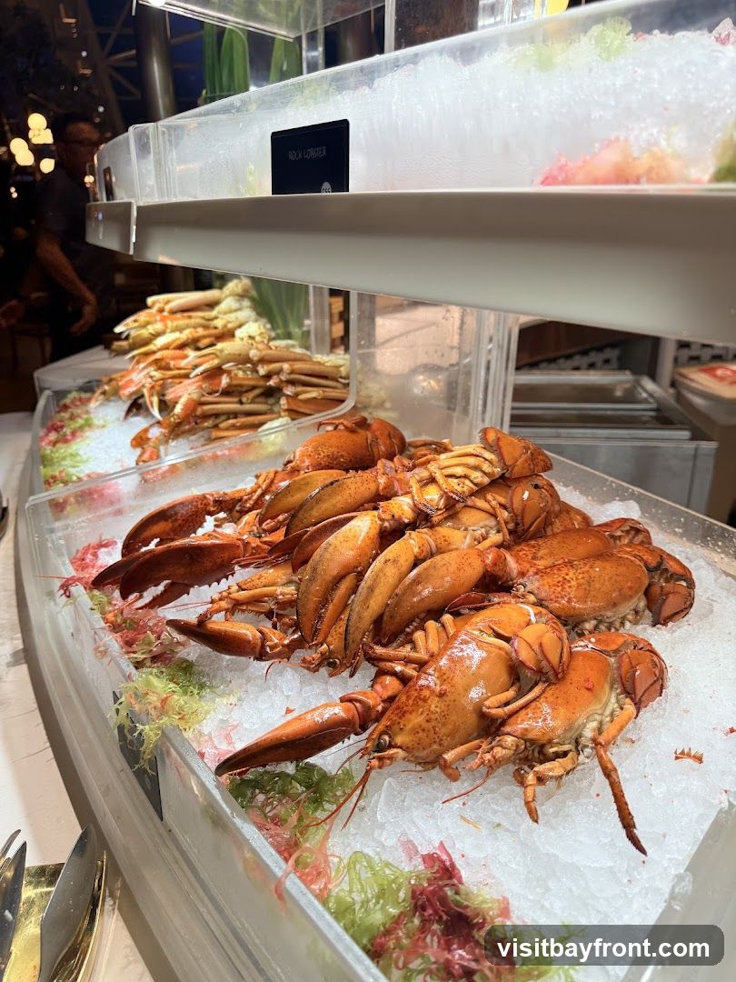 A close-up view of a seafood buffet display featuring several cooked lobsters on ice in the foreground. Behind them, rows of crab legs are also displayed on ice. A sign in the background reads "ROCK LOBSTER". The lighting suggests an indoor setting, possibly a restaurant or hotel.