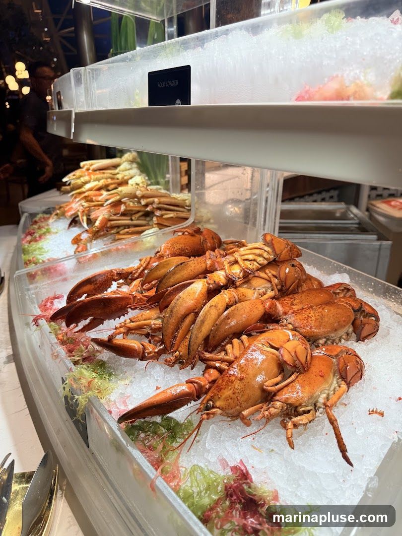 A close-up view of a seafood buffet display featuring several cooked lobsters on ice in the foreground. Behind them, rows of crab legs are also displayed on ice. A sign in the background reads "ROCK LOBSTER". The lighting suggests an indoor setting, possibly a restaurant or hotel.