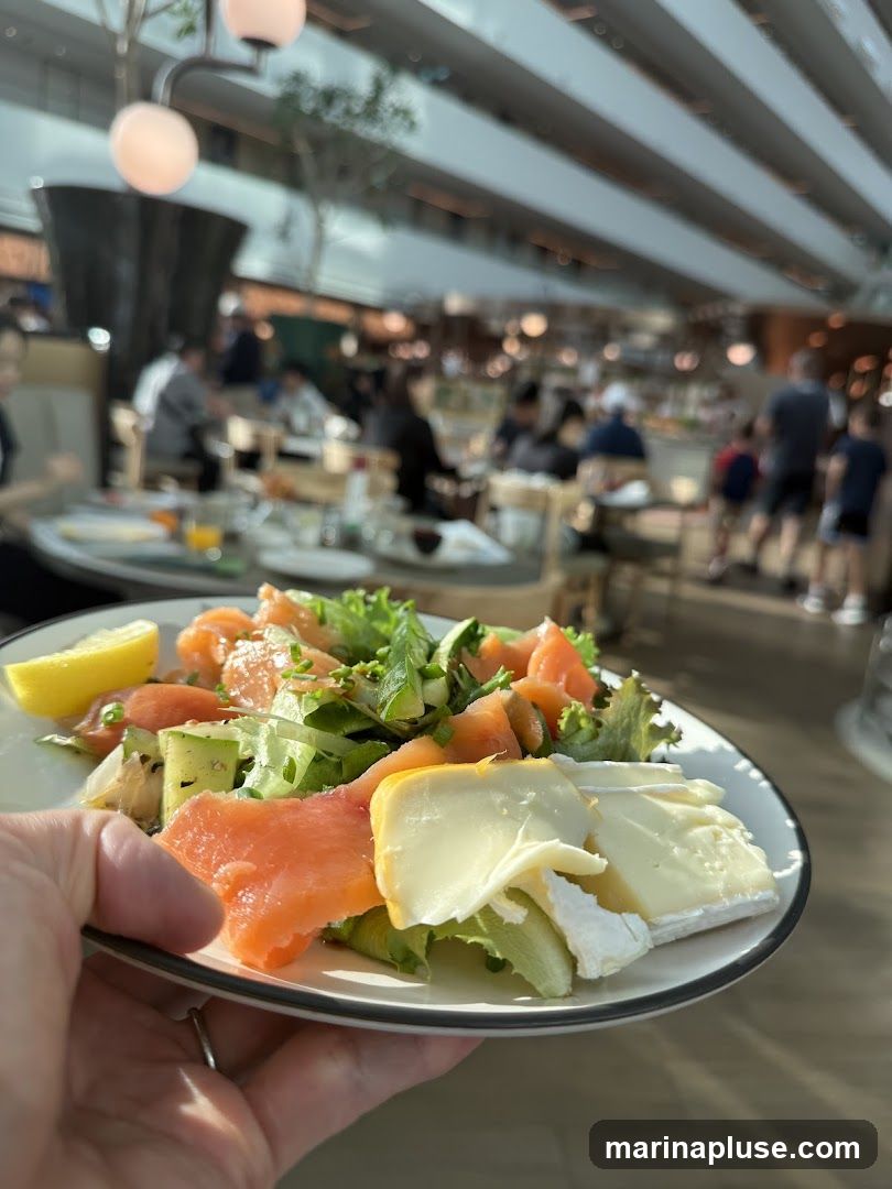 A close-up shot of a salad on a plate, held by a hand. The salad contains smoked salmon, lettuce, avocado, and cheese. In the background, a busy restaurant interior with people dining is visible.