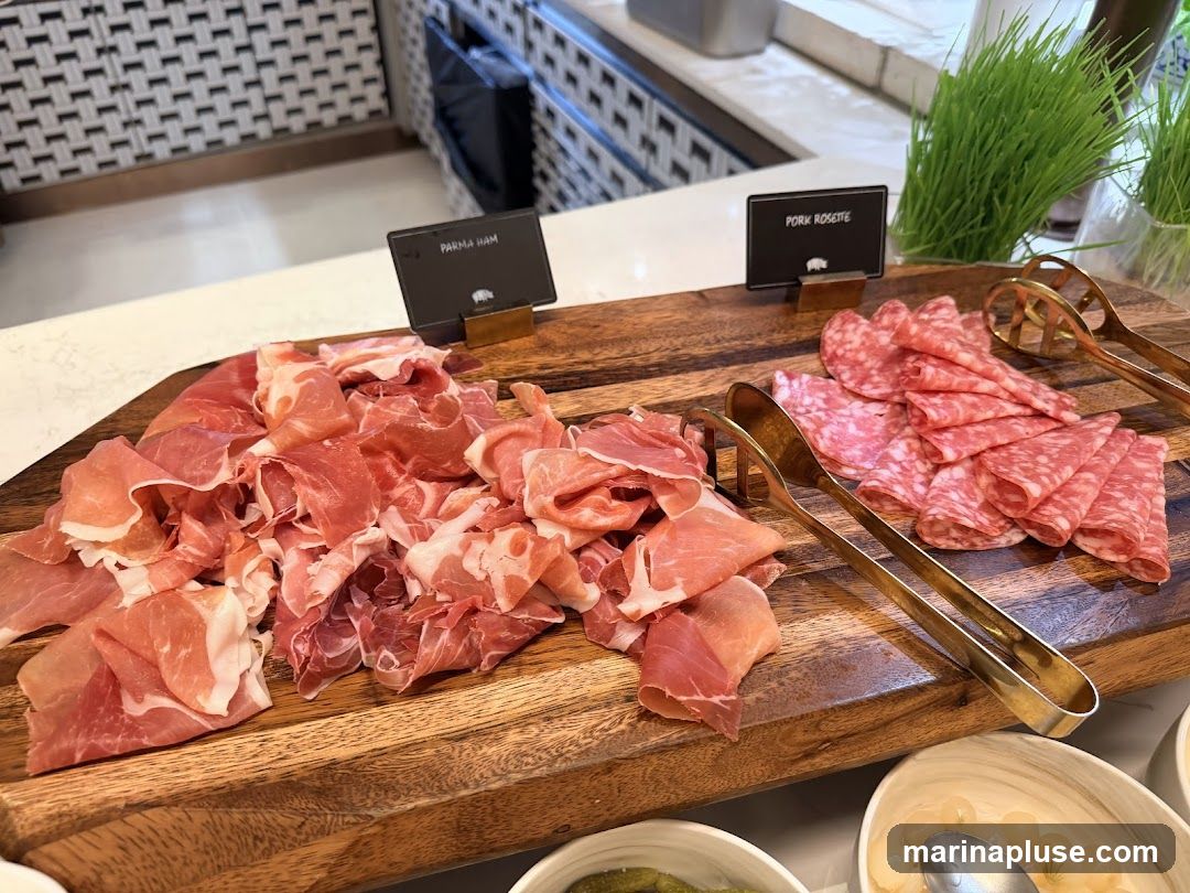 A wooden board displays thinly sliced Parma ham and Pork Rosette. Tongs are provided for serving. In the background, there are small potted plants and a patterned wall.
