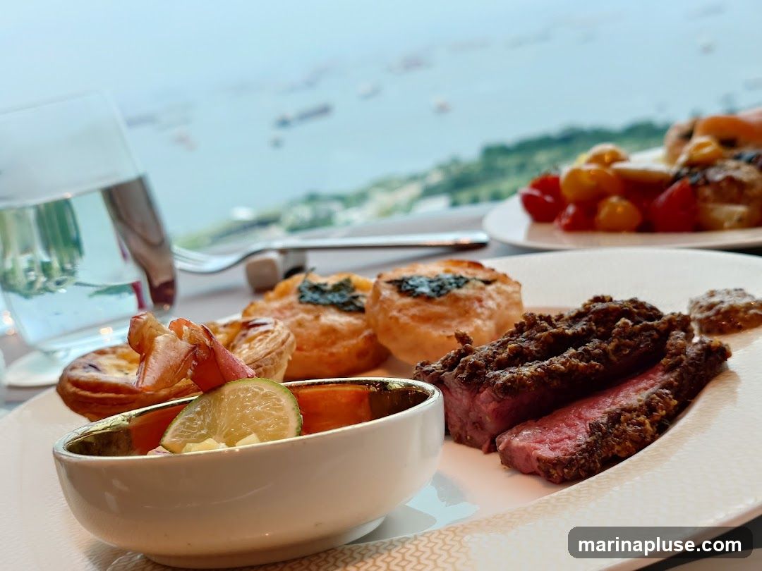 A close-up of a gourmet meal served on a white plate with a gold rim. The meal includes slices of medium-rare steak crusted with herbs, a small bowl with a lime wedge and what appears to be lobster meat, and two small savory tarts. In the background, another plate holds cherry tomatoes and other food items. A glass of water and cutlery are also visible. The setting appears to be a restaurant with a panoramic view of a bay dotted with ships.