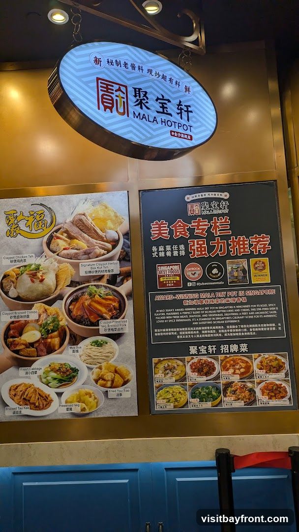 A sign displays a menu for Mala Hotpot, featuring various dishes with images and descriptions. The sign also highlights awards and recommendations for the restaurant. Dishes include Claypot Chicken Tea, Signature Claypot Herbal Bak Kut Teh, Claypot Braised Combo, Preserved Veg, Fresh Cabbage, and Fried You Tiao. A separate section showcases recommended dishes like Pickled Veg Paws, Spicy Chicken, Boiled Fish, and Stir-fried Intestine.