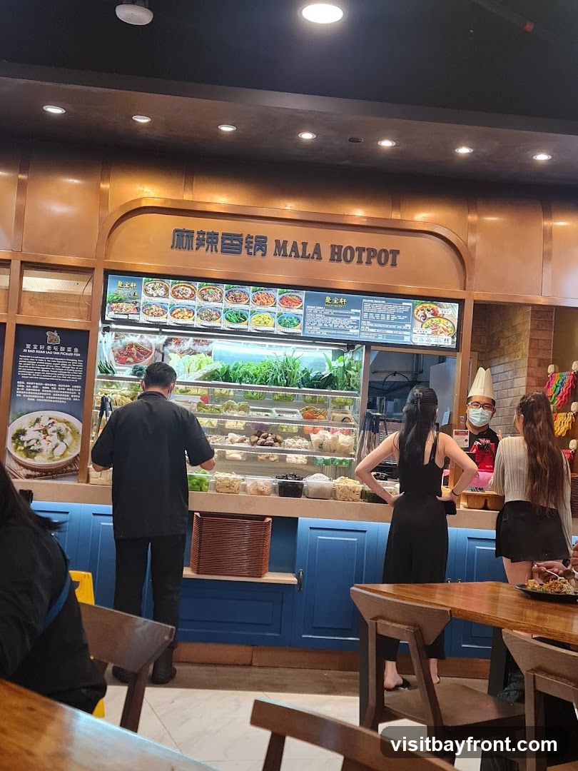 A counter display for Mala Hotpot with various ingredients and menu items visible. Staff members are attending to customers.