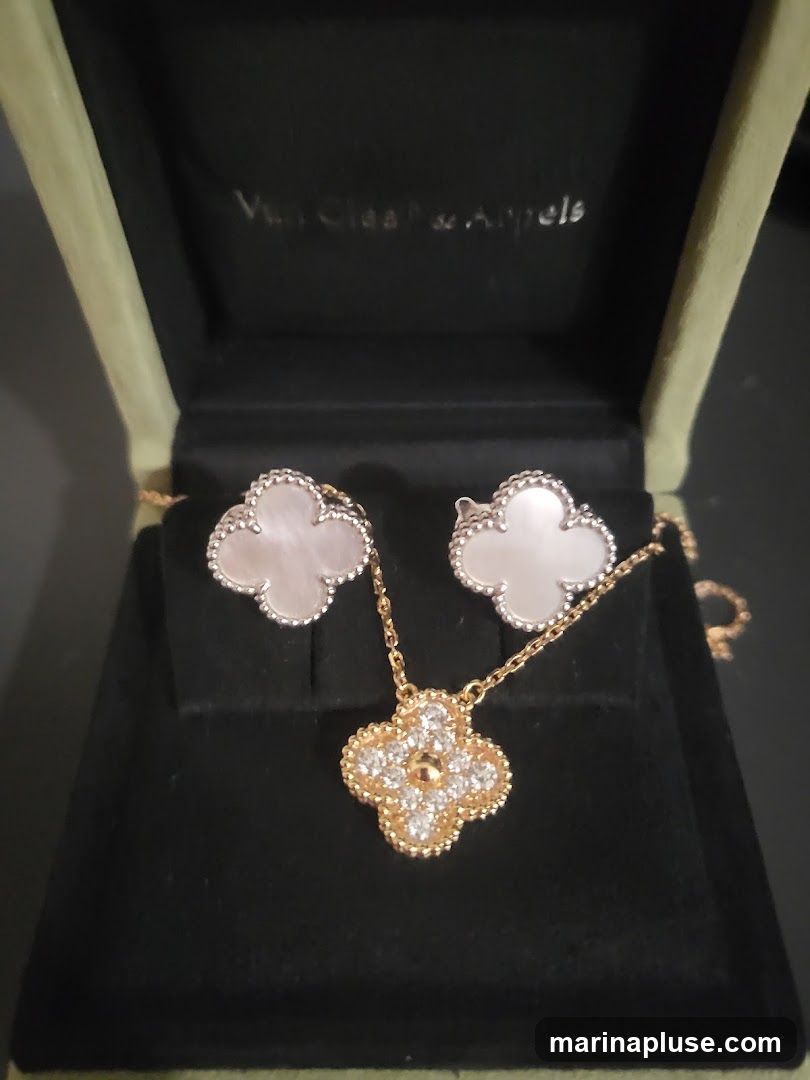 A close-up shot of a Van Cleef & Arpels jewelry set, including a necklace and a pair of earrings, displayed in a velvet-lined box. The necklace features a clover-shaped pendant adorned with diamonds, while the earrings are made of mother-of-pearl with a similar clover design. The brand's logo is visible on the inside lid of the box.
