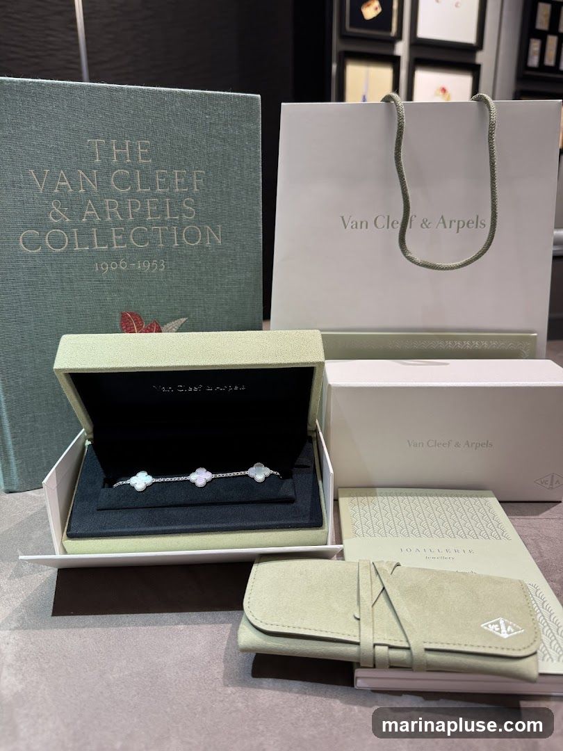 A collection of items from Van Cleef & Arpels, including a book titled "The Van Cleef & Arpels Collection 1906-1953", a shopping bag, a jewelry box containing a bracelet with clover motifs, a jewelry case, and a booklet.