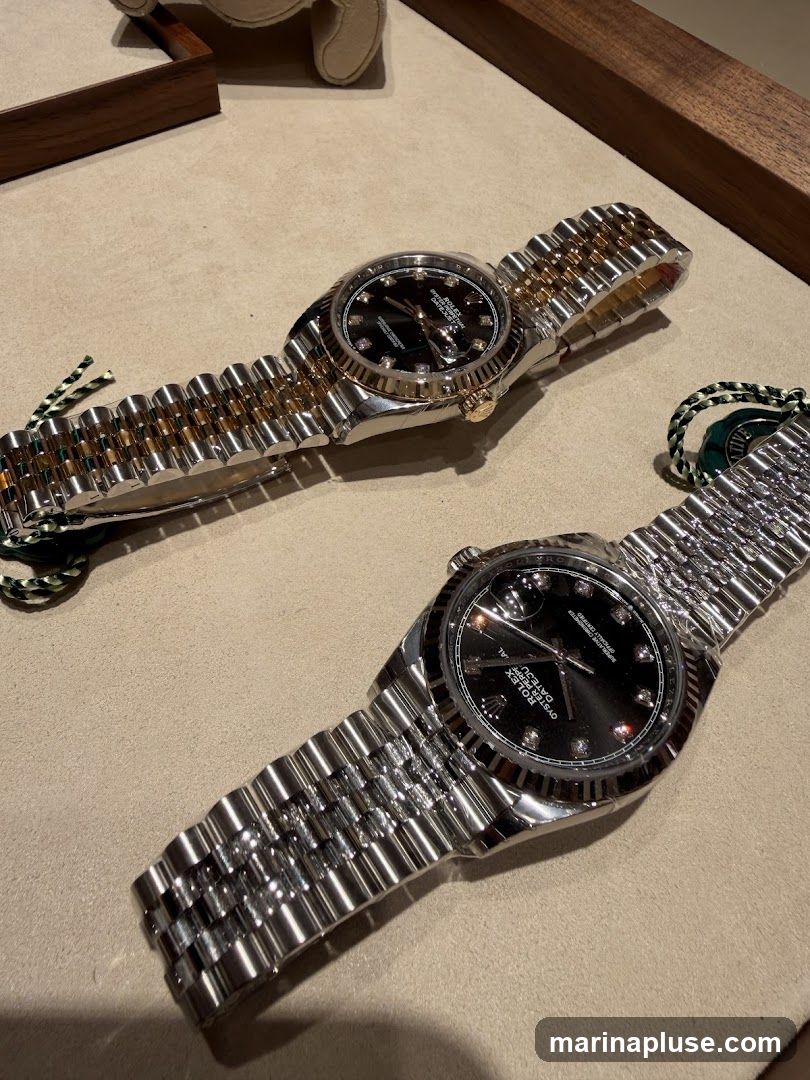 Two Rolex watches are displayed on a beige surface. The watch in the foreground is made of stainless steel with a black dial and diamond hour markers. The watch in the background has a two-tone band, combining stainless steel and gold, and also features a black dial with diamond hour markers. Both watches have the Rolex logo and "Oyster Perpetual Datejust" text visible on their dials.