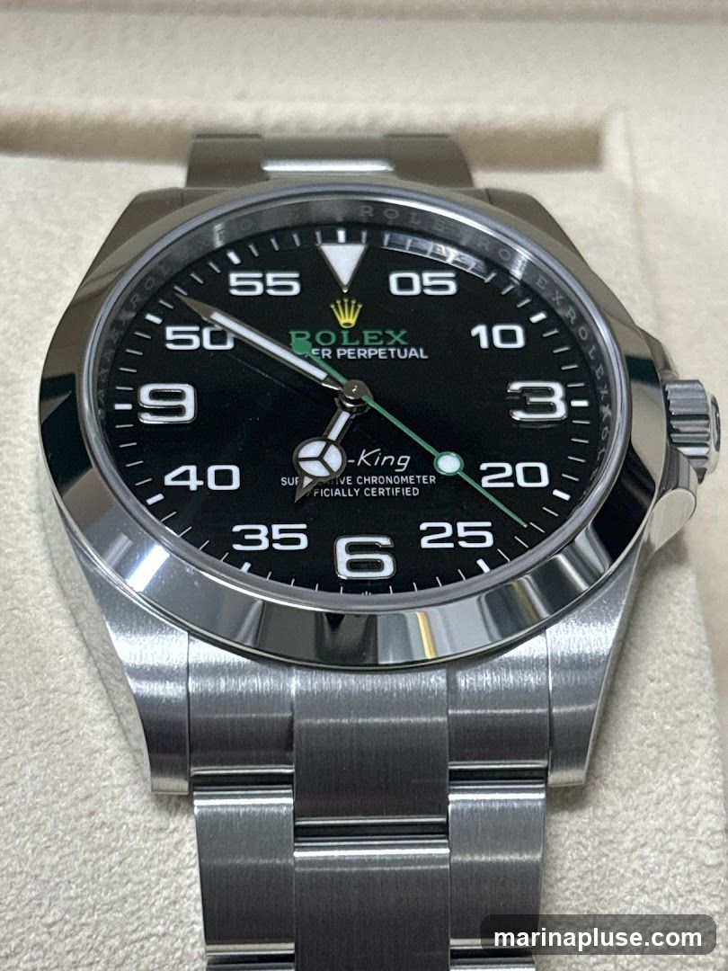 A close-up, detailed photograph of a Rolex Air-King wristwatch with a black dial. The watch features a stainless steel case and bracelet. The dial displays Arabic numerals for hours 3, 6, and 9, with markers for other hours. The Rolex logo and "PERPETUAL" are visible in green text. The text "AIR-KING" and "SUPERLATIVE CHRONOMETER OFFICIALLY CERTIFIED" are also present on the dial. The watch is presented in a light-colored box.