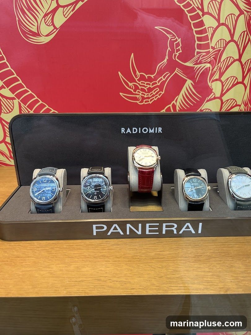 A display of five Panerai watches, with the brand name "PANERAI" visible on a metallic strip below the watches. Above the watches, the word "RADIOMIR" is displayed. The background features a red surface with a gold dragon design. The watches are presented on individual stands within a dark display case.