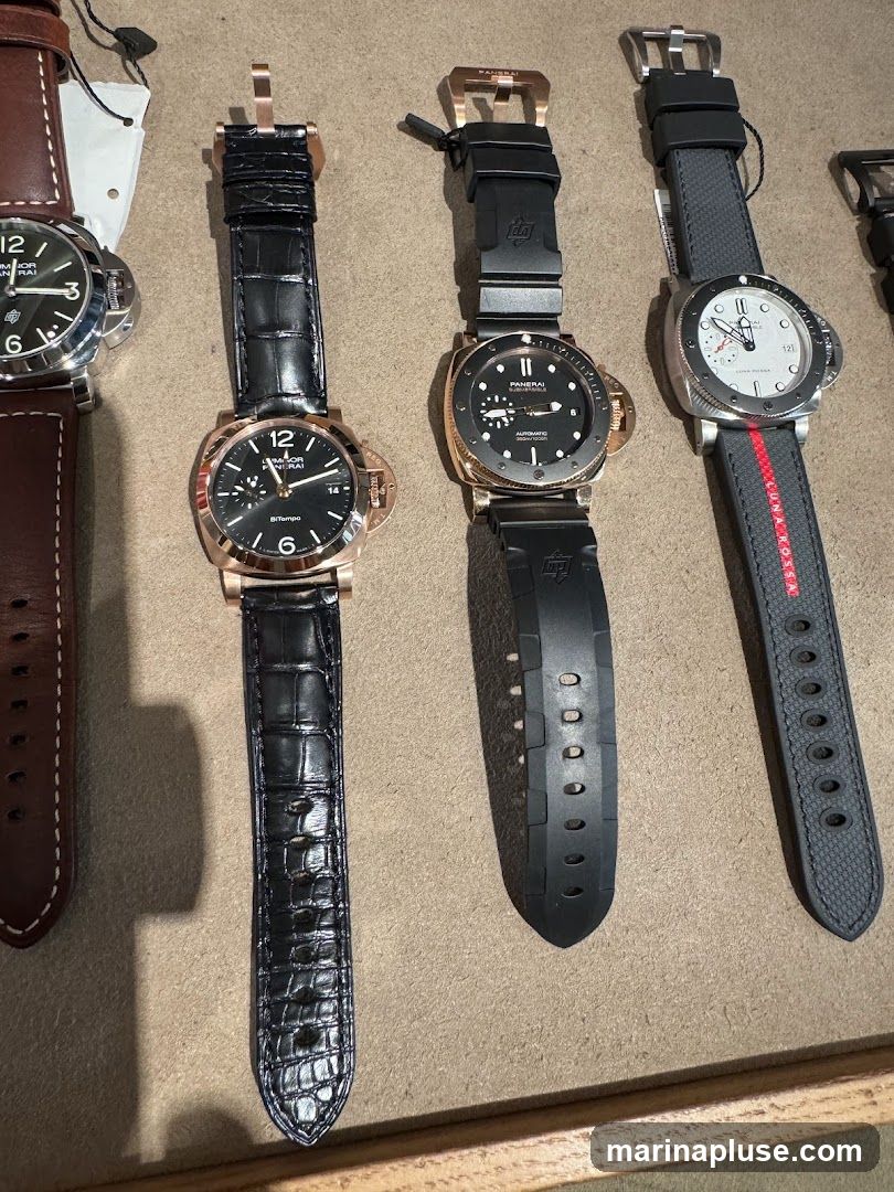 A close-up overhead view of four Panerai watches displayed on a textured surface. The watches feature various strap materials including black alligator leather, black rubber, and a grey fabric strap with red and black stripes. The watch faces are visible, showing different dial designs and complications.