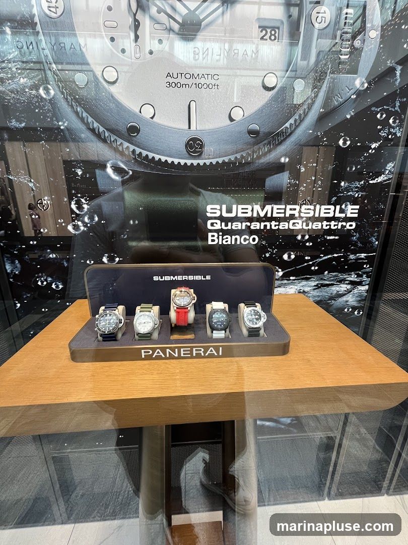 A display of five Panerai Submersible watches on a wooden stand, with a large promotional image of a watch face and water droplets in the background. The watches have various strap colors including blue, green, red, and black. The brand name 'PANERAI' is visible on the display stand.