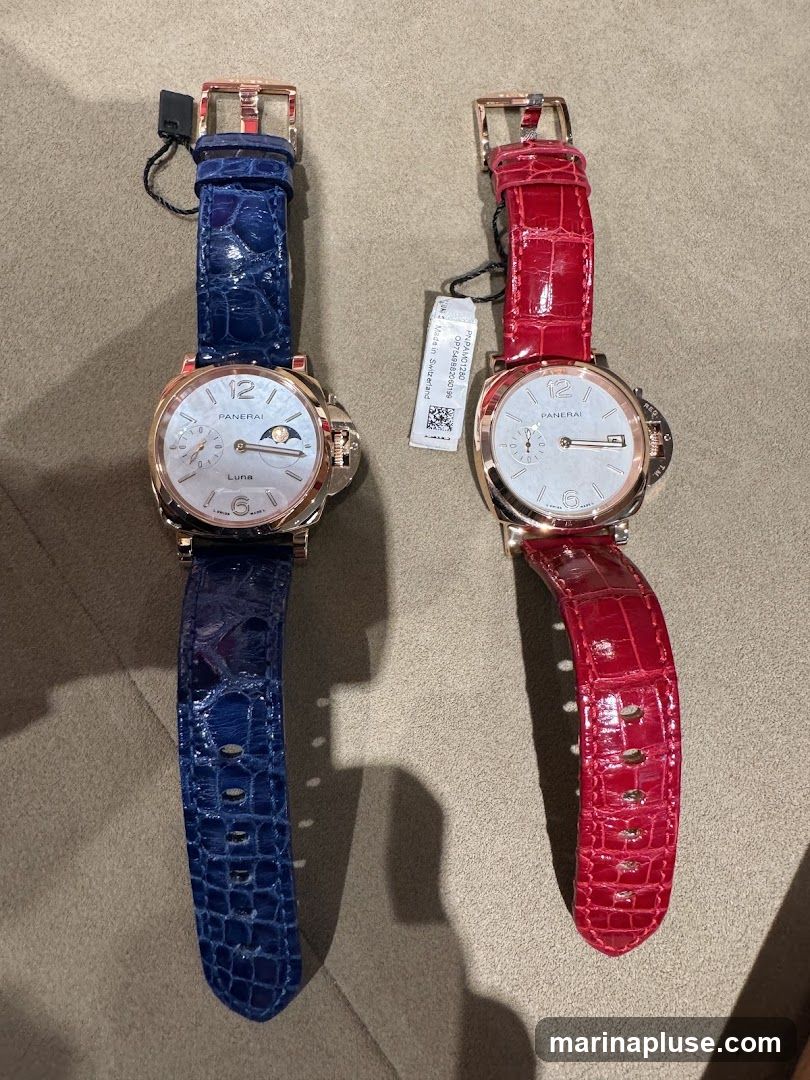 A top-down view of two Panerai watches with rose gold cases and alligator leather straps. The watch on the left has a blue strap and a white dial with a moon phase complication. The watch on the right has a red strap and a white dial. Both watches have the Panerai logo and "Luna" visible on their dials.