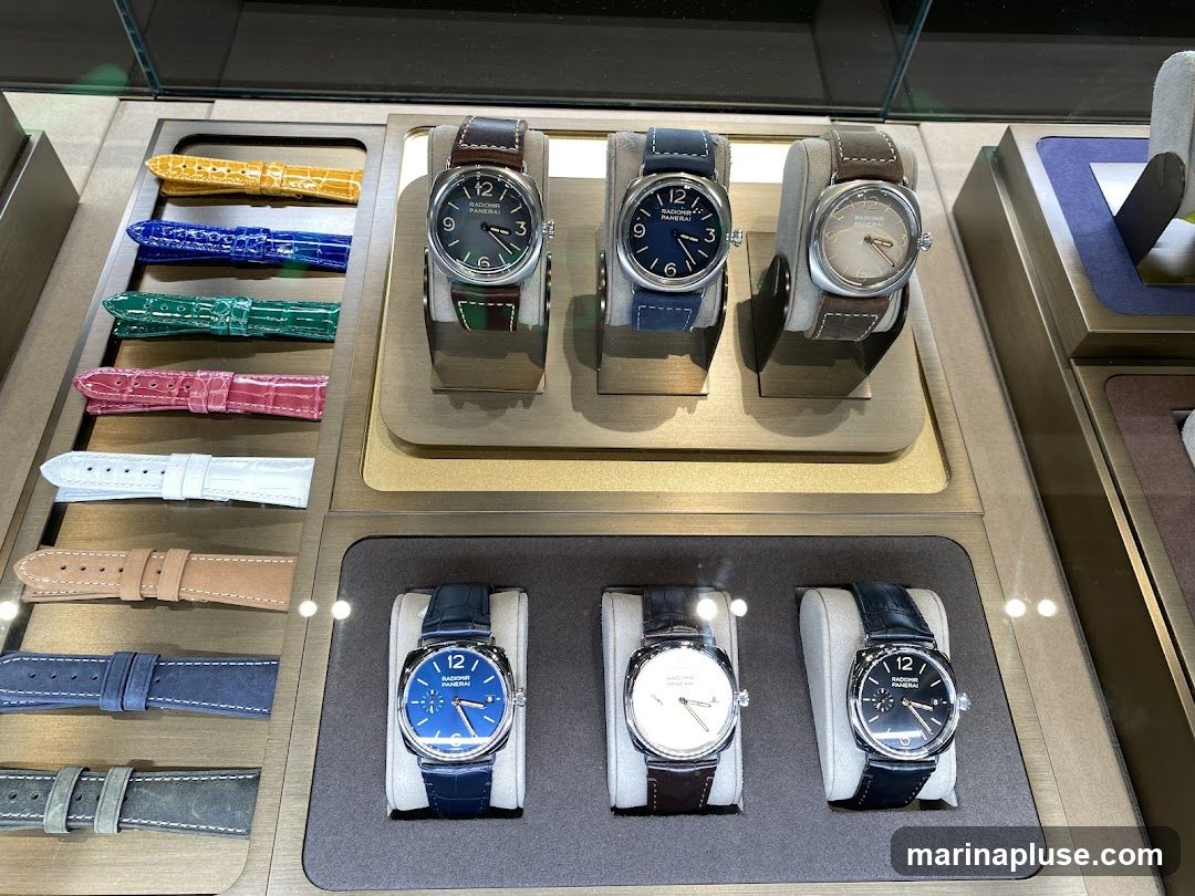 A display case featuring several luxury watches and an assortment of colorful watch straps. The watches are arranged on stands, with some showing different dial colors and strap materials. The watch straps are laid out in rows, showcasing a variety of colors including yellow, blue, green, pink, white, tan, grey, and dark blue.